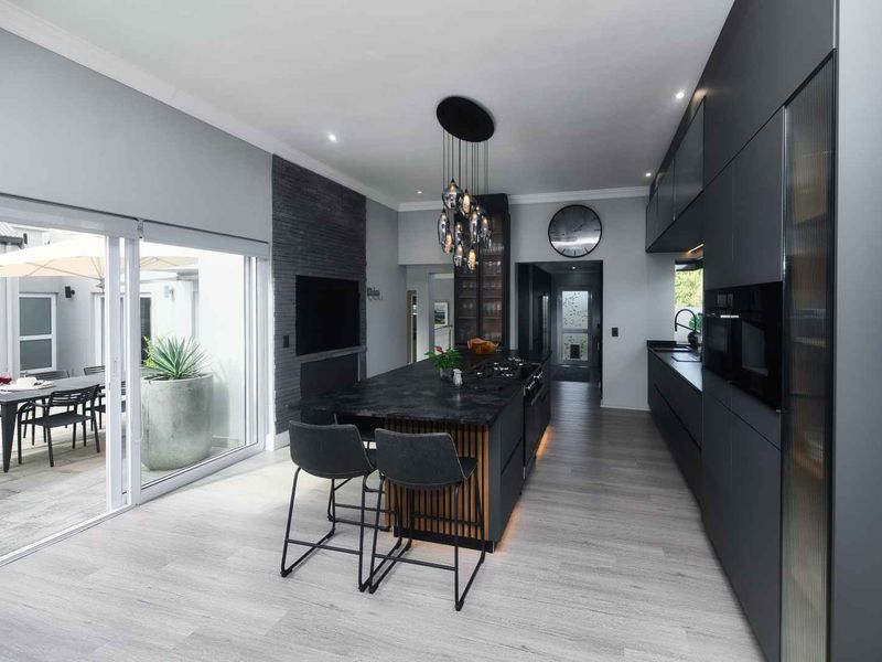 Modern open-plan kitchen featuring a large central island, sleek dark cabinetry, integrated appliances, and seamless flow to the outdoor patio area.