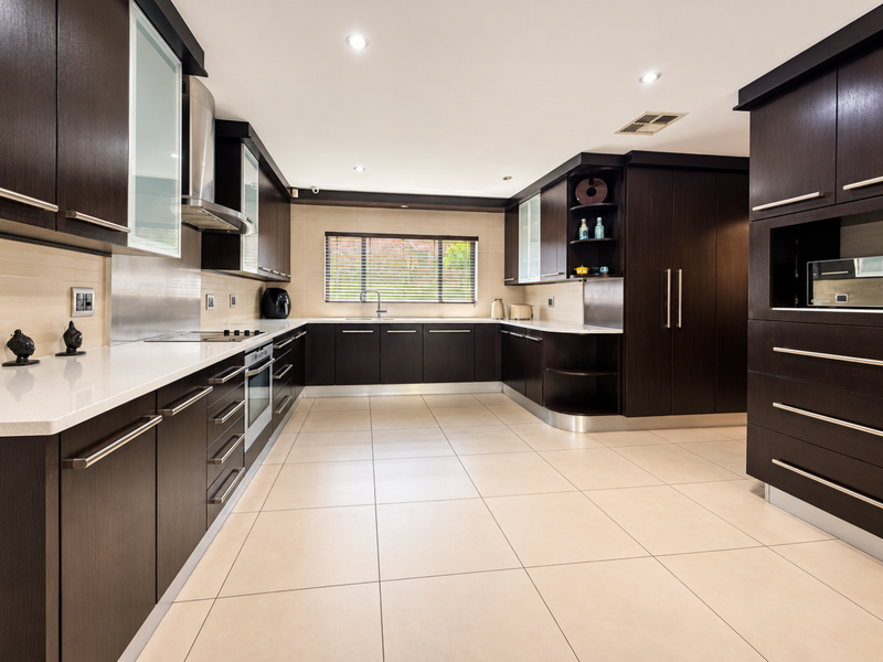Modern kitchen featuring dark wood cabinetry, stone countertops, integrated appliances, and large format floor tiles with ample storage space.