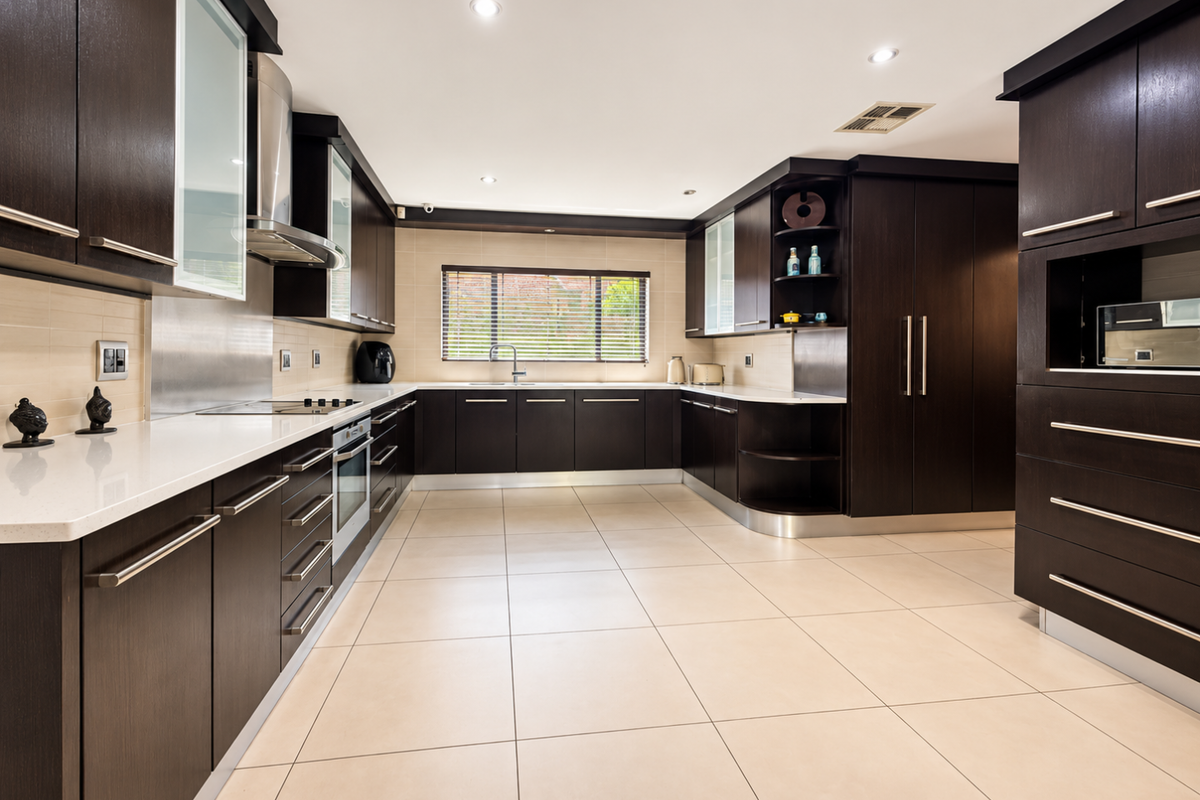 Modern kitchen featuring dark wood cabinetry, stone countertops, integrated appliances, and large format floor tiles with ample storage space.