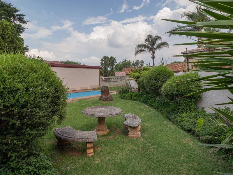 A private backyard featuring a swimming pool, established garden landscaping, and secure perimeter walling with electric fencing.
