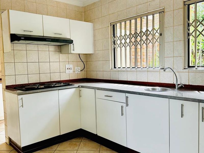 A functional kitchen featuring white cabinetry, laminate countertops, a built-in hob with extractor fan, and tiled flooring with security bars on the windows.