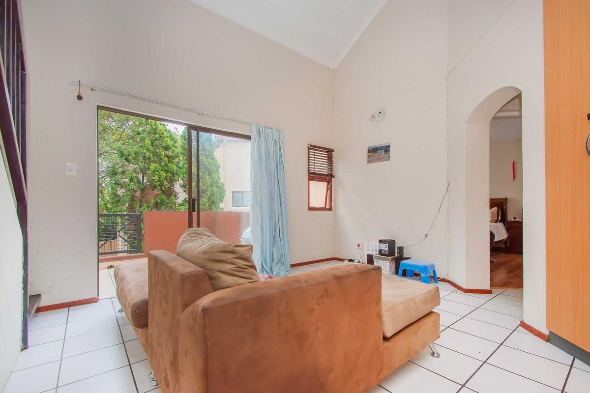 Spacious living area featuring high vaulted ceilings, tiled flooring, and sliding glass doors providing access to an outdoor balcony.