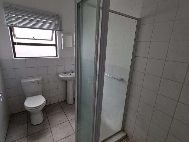 A functional bathroom featuring a shower enclosure, pedestal basin, and toilet with tiled finishes throughout.