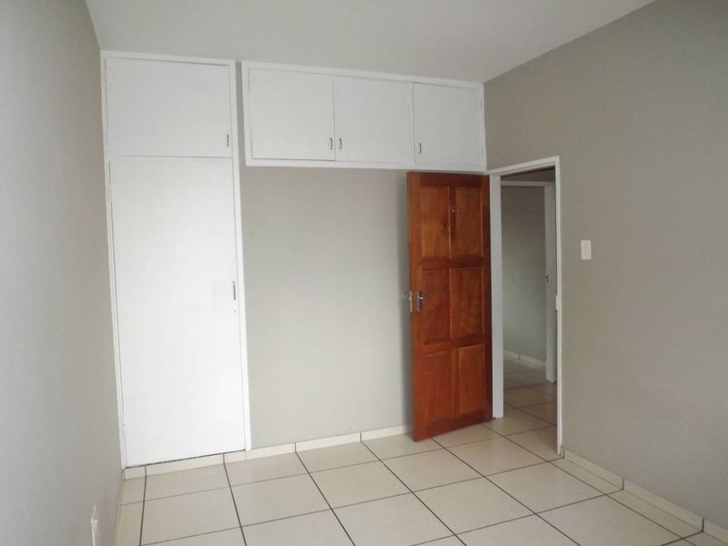 An empty bedroom featuring tiled flooring, built-in cupboards with overhead storage, and a solid wooden door.