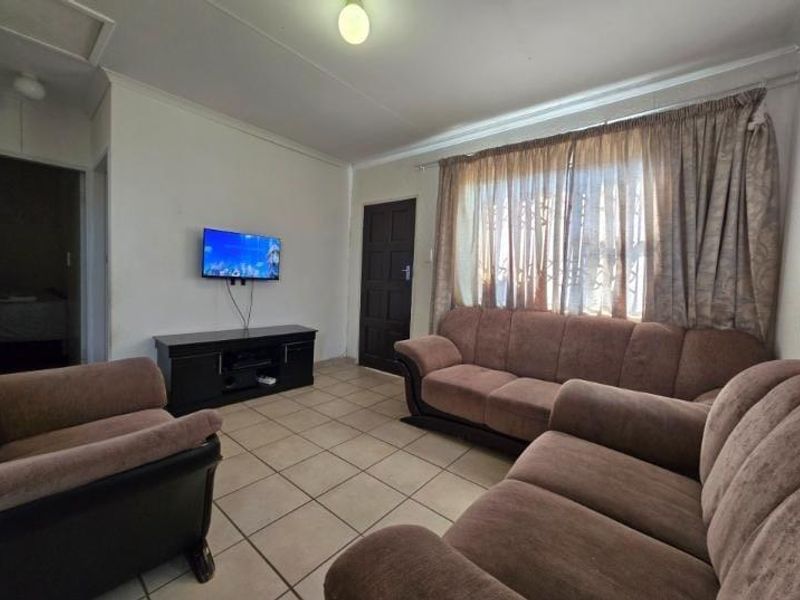 A functional living room featuring tiled flooring, neutral walls, and natural light through window curtains.