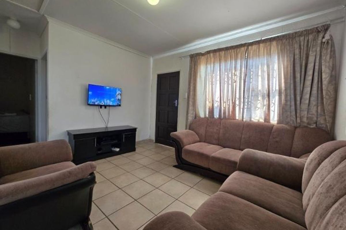 A functional living room featuring tiled flooring, neutral walls, and natural light through window curtains.