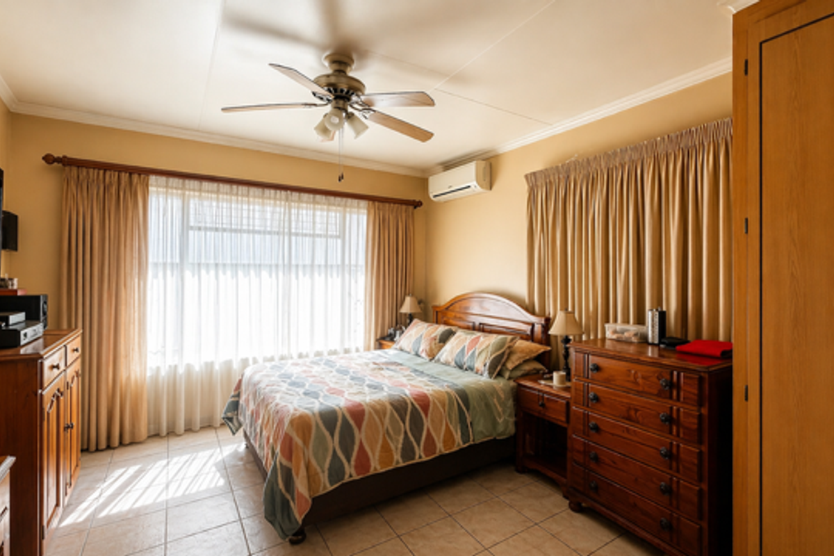 A well-maintained bedroom featuring tiled flooring, a ceiling fan, and a wall-mounted air conditioning unit, providing a comfortable and functional living space.
