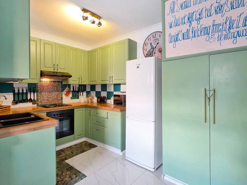 A vibrant kitchen featuring green cabinetry, timber countertops, a tiled splashback, and modern tiled flooring, offering a functional and characterful cooking space.