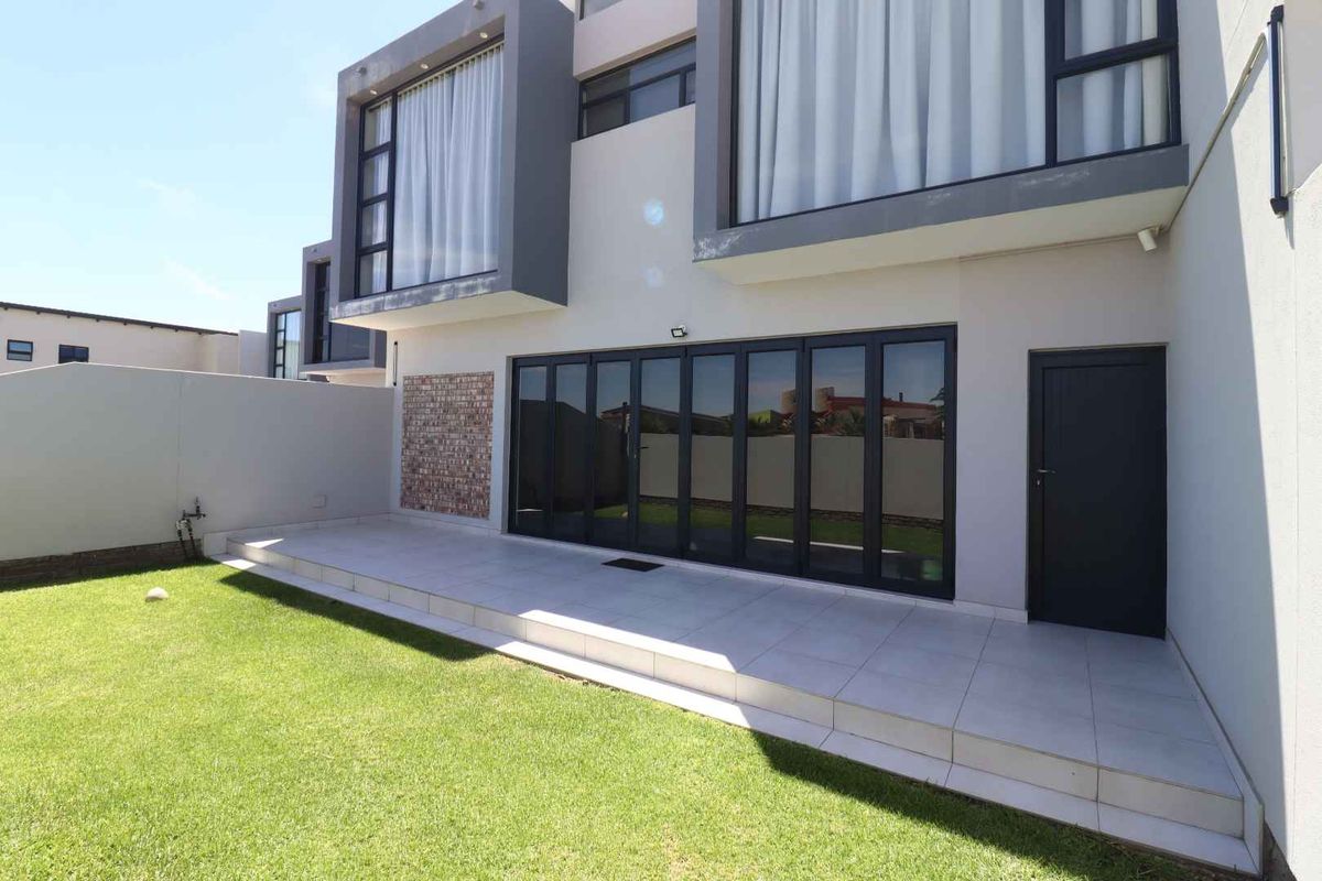 Modern townhouse rear elevation featuring a tiled patio, large black-framed folding glass doors, and a well-maintained private garden.