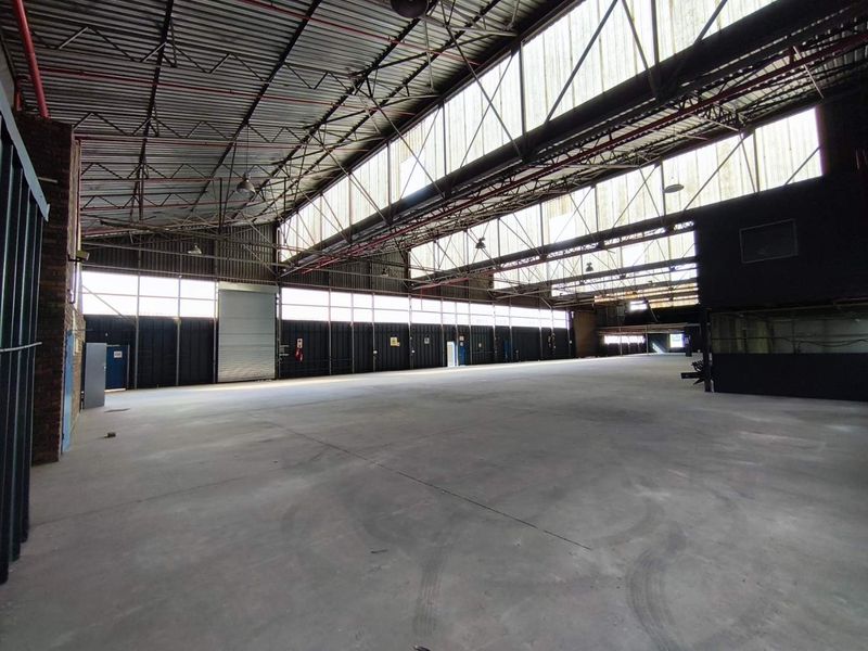 Expansive industrial warehouse space featuring high ceilings with exposed steel trusses, clerestory windows for natural light, and durable concrete flooring.