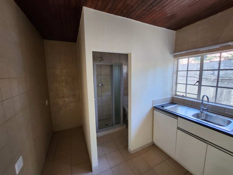 A functional kitchen area featuring built-in cabinetry, a stainless steel sink, and an adjacent enclosed shower space with dated finishes.