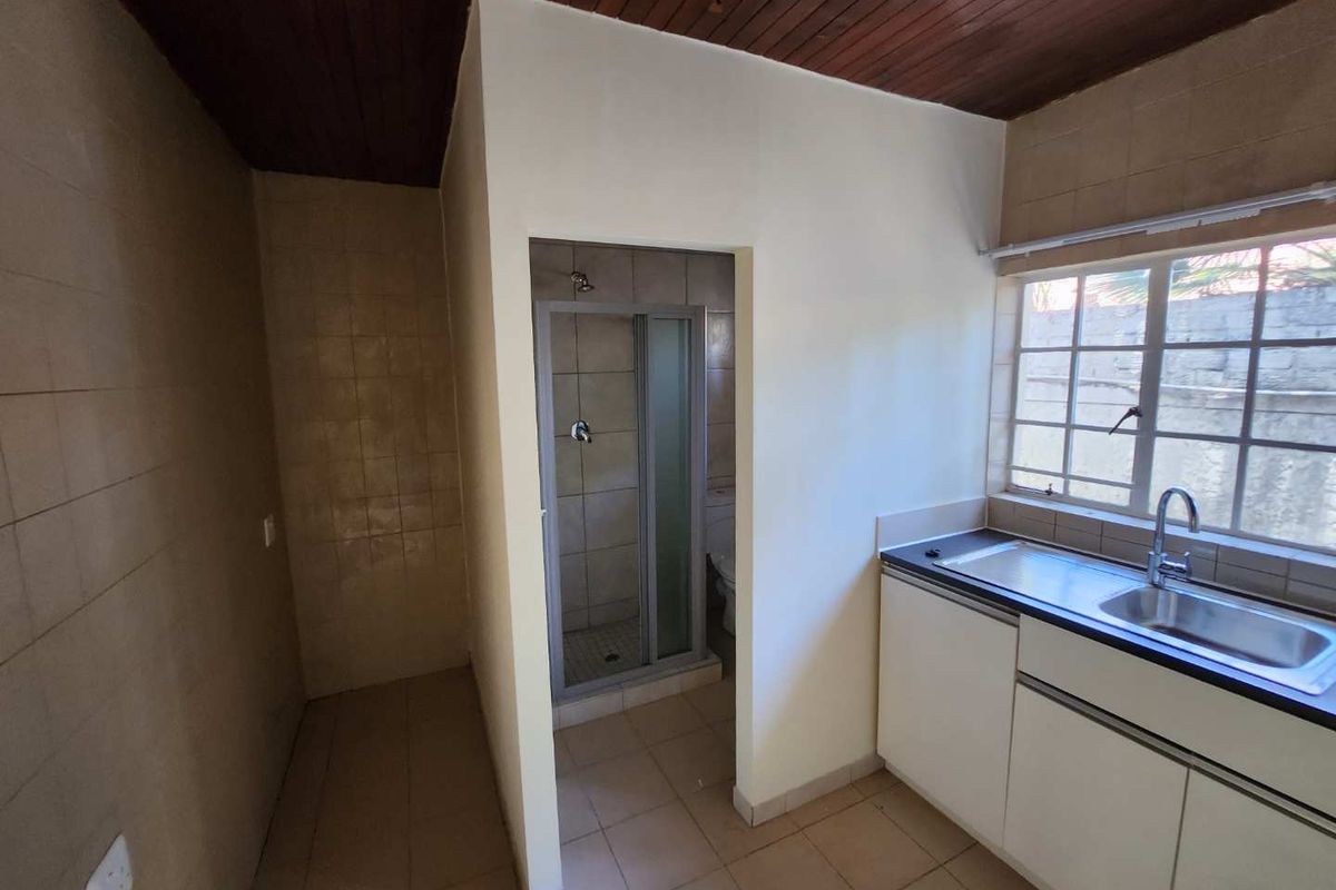 A functional kitchen area featuring built-in cabinetry, a stainless steel sink, and an adjacent enclosed shower space with dated finishes.