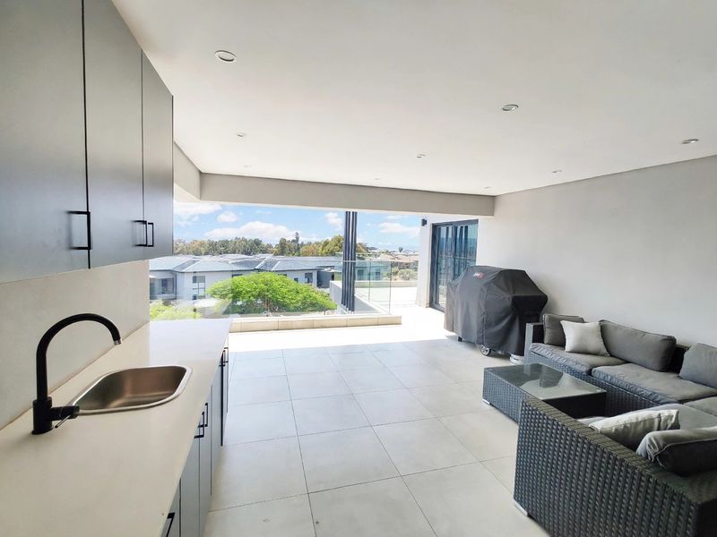 Spacious covered balcony featuring a built-in kitchenette with sink, modern cabinetry, and a glass balustrade offering expansive outdoor views.