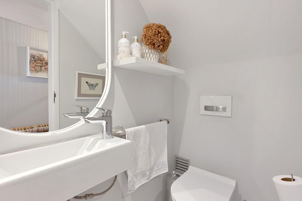 A compact, modern bathroom featuring a wall-mounted toilet with a concealed cistern, a sleek vanity basin, and a contemporary mirror.