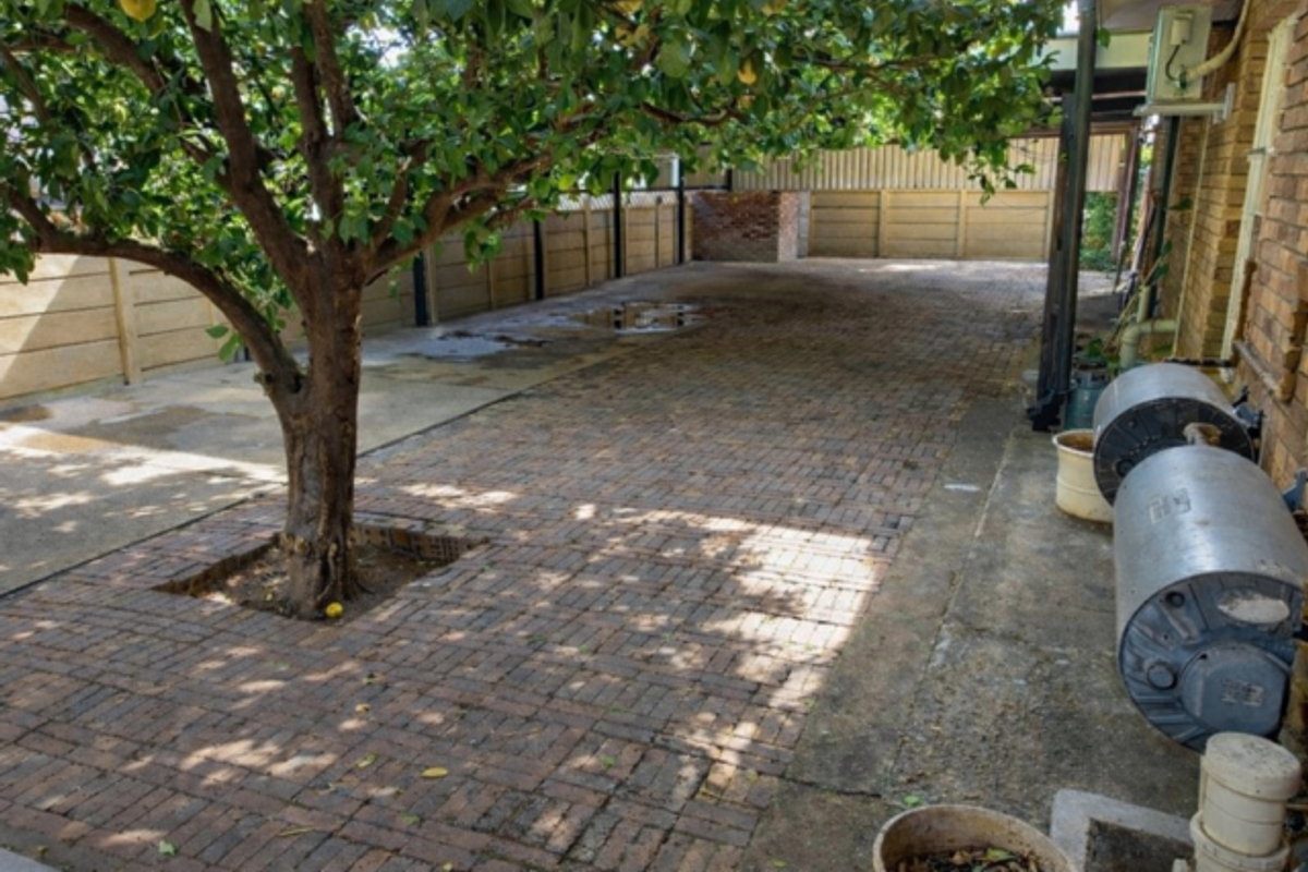 A paved rear courtyard area featuring a mature tree, perimeter fencing, and external water heating units attached to the brick building wall.