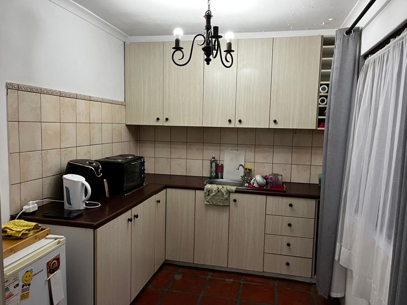 A compact kitchen featuring laminate cabinetry, tiled backsplash, and terracotta flooring, with visible signs of ceiling water damage requiring attention.