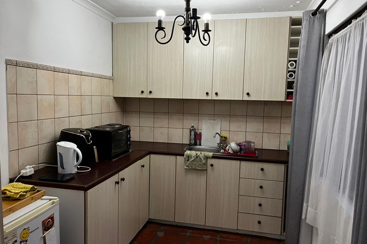 A compact kitchen featuring laminate cabinetry, tiled backsplash, and terracotta flooring, with visible signs of ceiling water damage requiring attention.