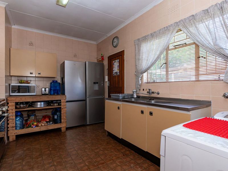 A functional kitchen featuring dated cabinetry, tiled splashbacks, a stainless steel sink, and a gas stove, offering potential for a modern renovation.