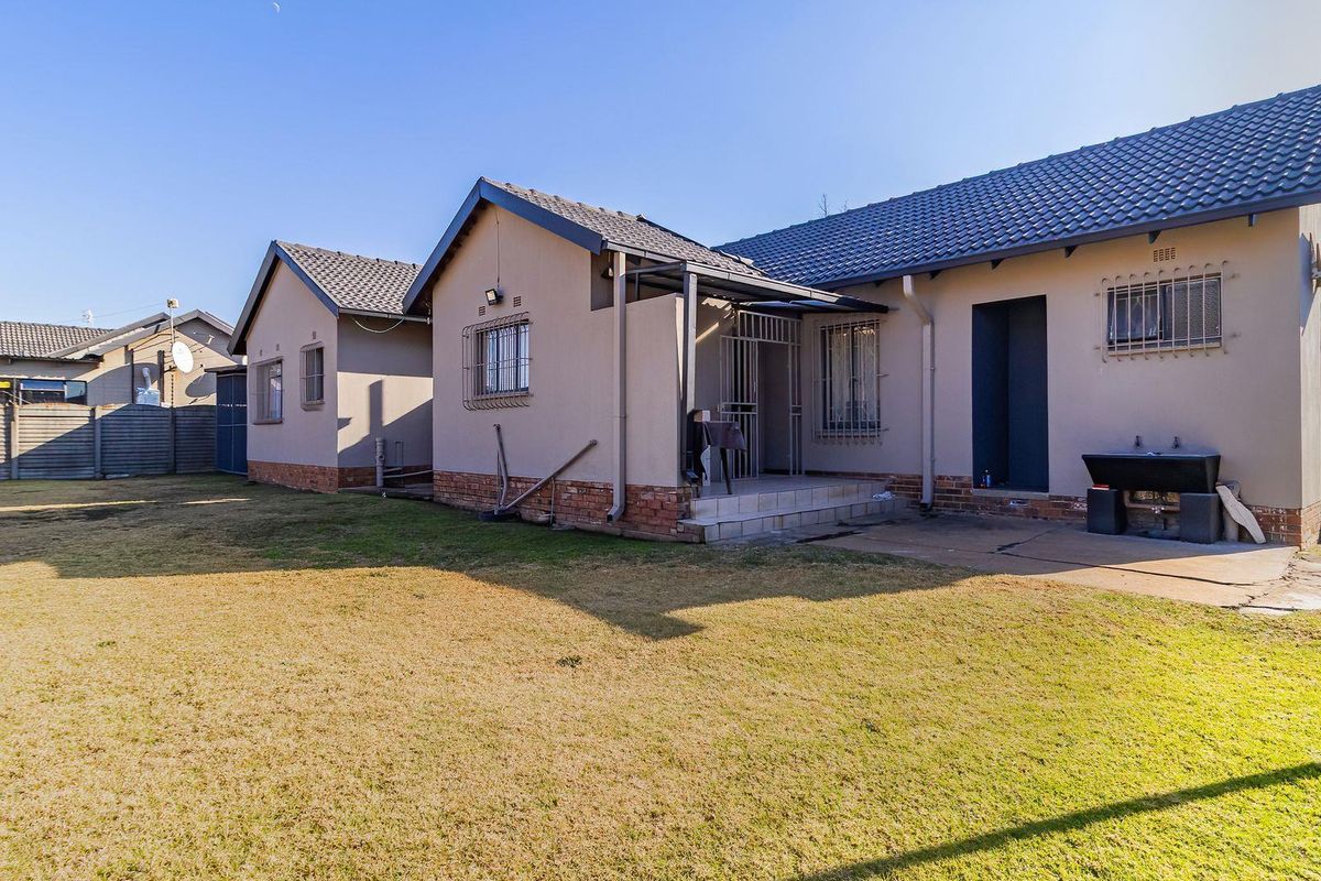 Rear view of the house featuring a tiled roof, security bars on windows, and a concrete patio area overlooking the backyard lawn.