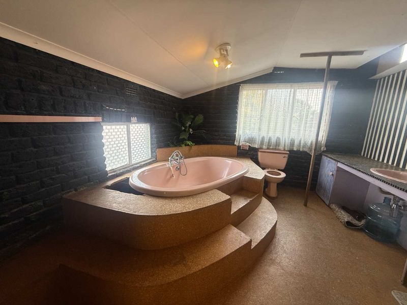 A unique bathroom featuring a raised, built-in pink bathtub, matching toilet, and vanity, set against dark textured brick walls.