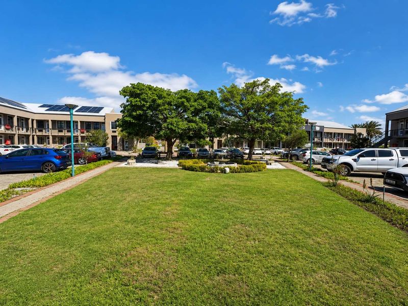 A well-maintained office park courtyard featuring a central lawn, mature trees, a water feature, and surrounding office buildings with solar panel installations.