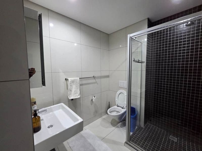 Modern bathroom featuring a wall-mounted basin, a wall-hung toilet, and a glass-enclosed shower with dark mosaic tiling.