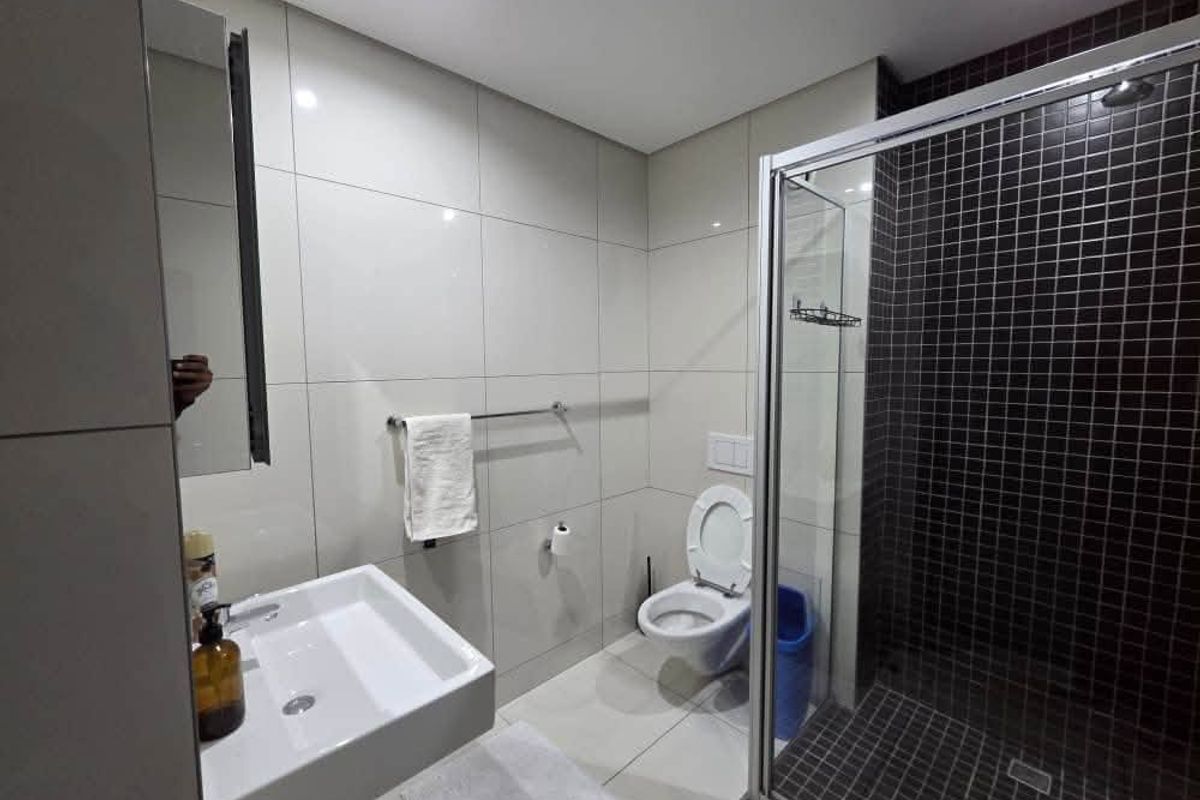 Modern bathroom featuring a wall-mounted basin, a wall-hung toilet, and a glass-enclosed shower with dark mosaic tiling.