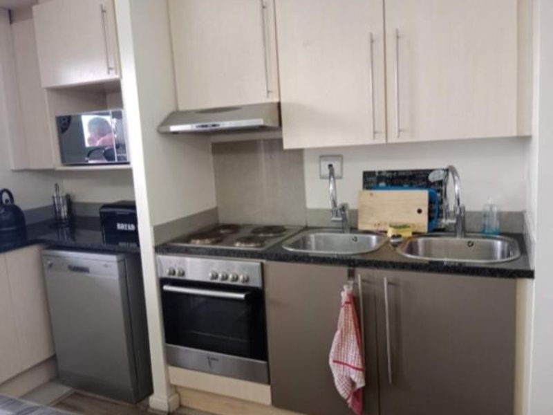 Compact kitchen featuring light-toned cabinetry, granite countertops, a double sink, and built-in appliances including an oven, hob, and extractor fan.