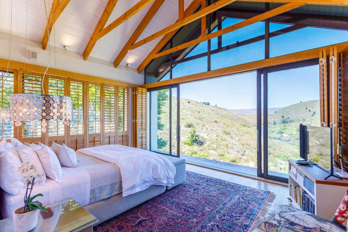 Spacious bedroom featuring vaulted timber-beamed ceilings, large sliding glass doors, and expansive views of the surrounding landscape.