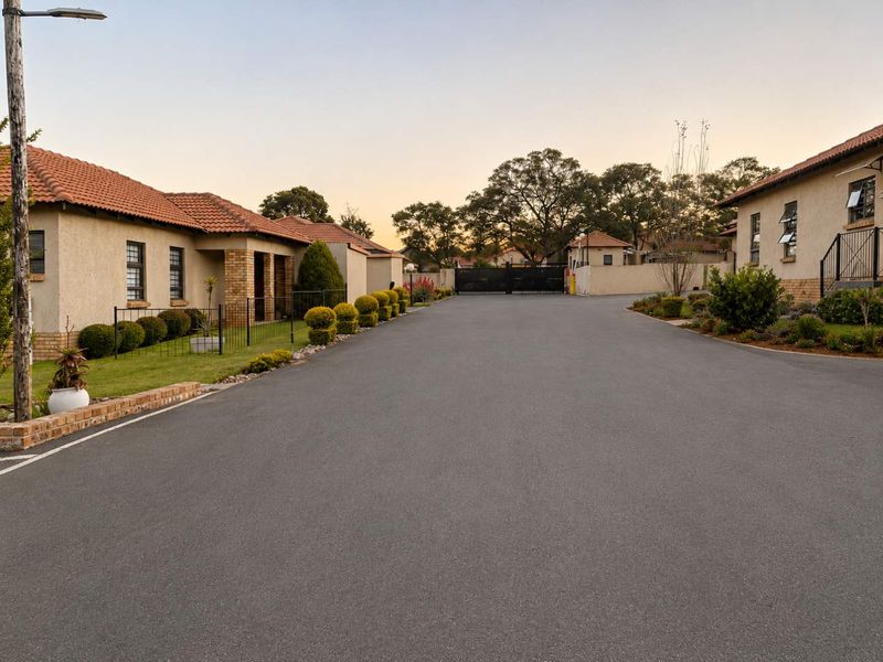 A view of the complex driveway and entrance, featuring well-maintained townhouse facades with terracotta roof tiles and secure gated access.