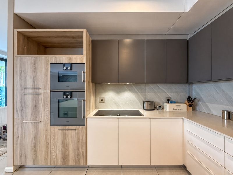 Modern kitchen featuring sleek two-tone cabinetry, integrated appliances including an oven and microwave, stone countertops, and a stylish tiled backsplash.