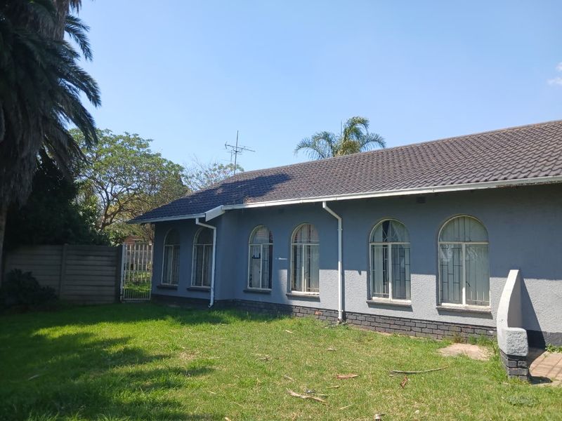 Rear elevation of the house featuring a tiled roof, arched windows with security bars, and a surrounding garden area.