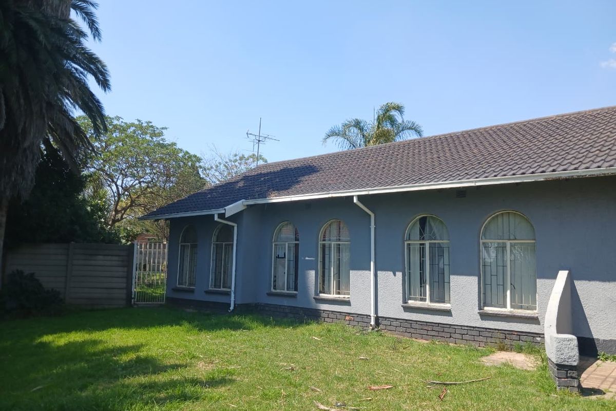 Rear elevation of the house featuring a tiled roof, arched windows with security bars, and a surrounding garden area.