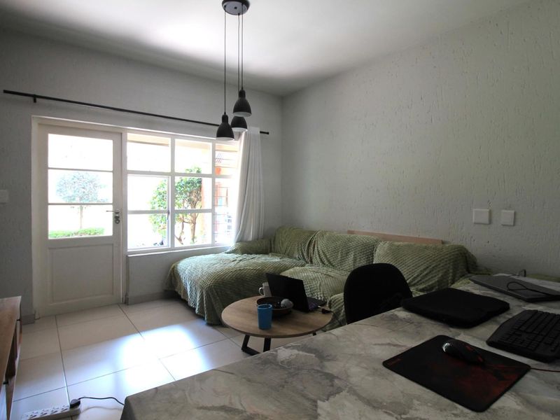 A living room featuring tiled flooring, textured walls, and a glass door providing natural light and access to the exterior.