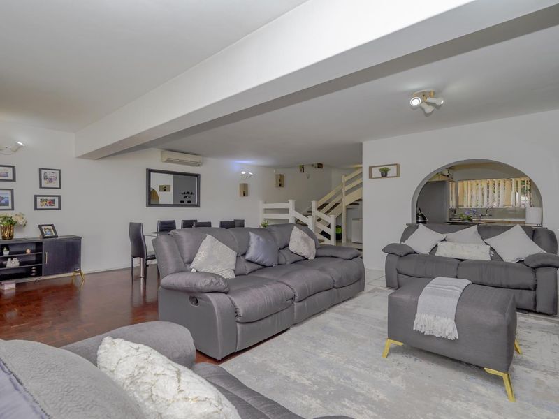 Spacious open-plan living and dining area featuring parquet flooring, a central staircase, and an arched opening leading to the kitchen.
