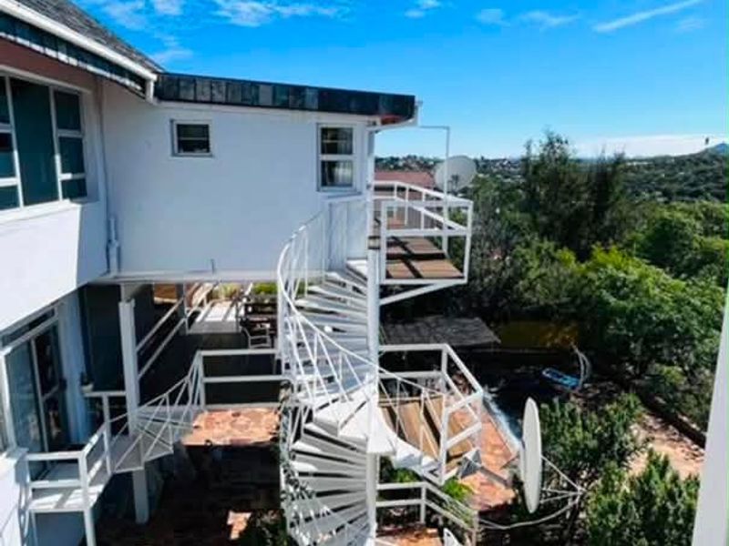Rear exterior view featuring a white spiral staircase connecting multiple levels, stone paving, and a raised wooden deck overlooking the garden.