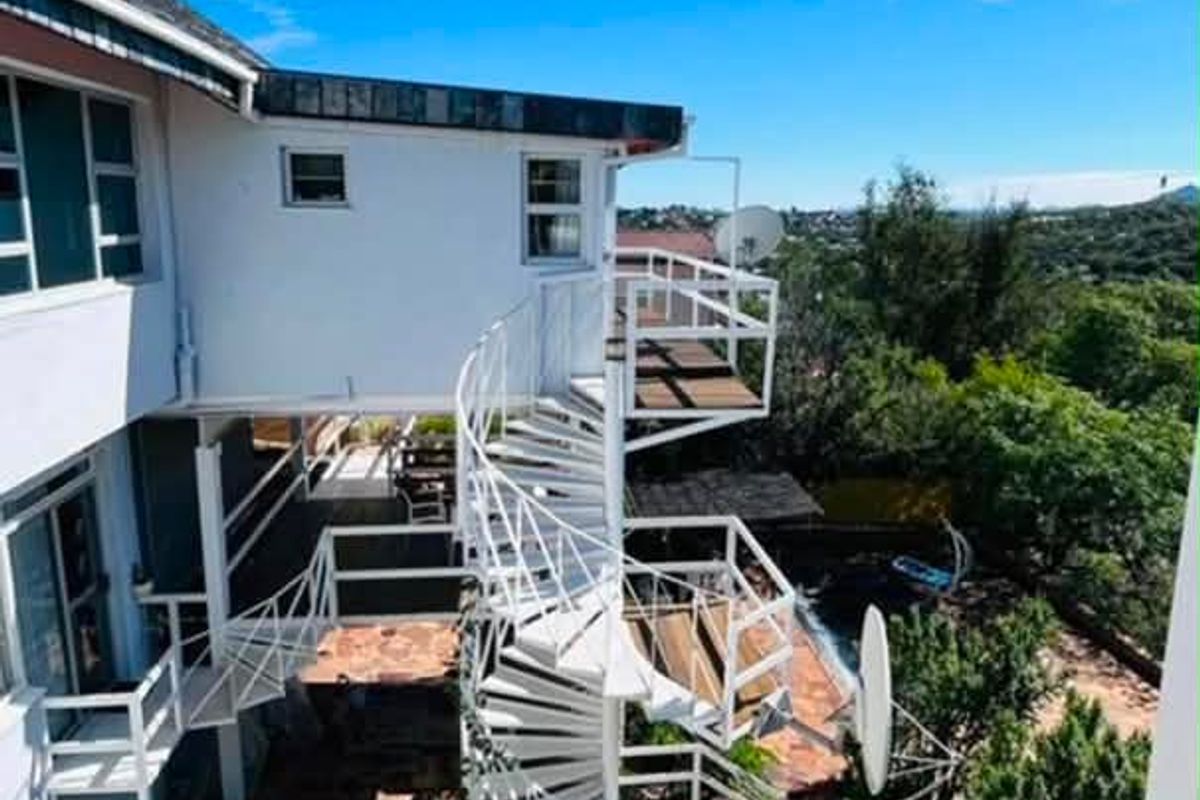 Rear exterior view featuring a white spiral staircase connecting multiple levels, stone paving, and a raised wooden deck overlooking the garden.