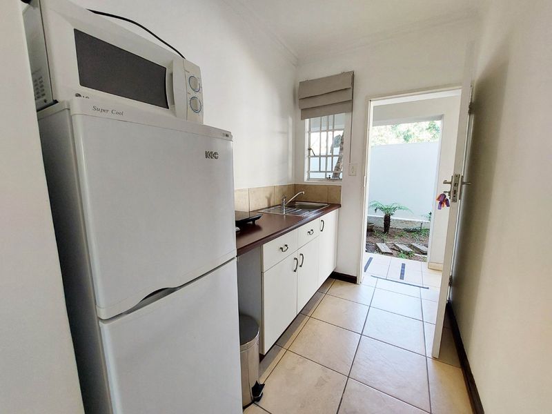 Compact scullery area featuring built-in cabinetry, a stainless steel sink, and direct access to an outdoor space through a secure door.
