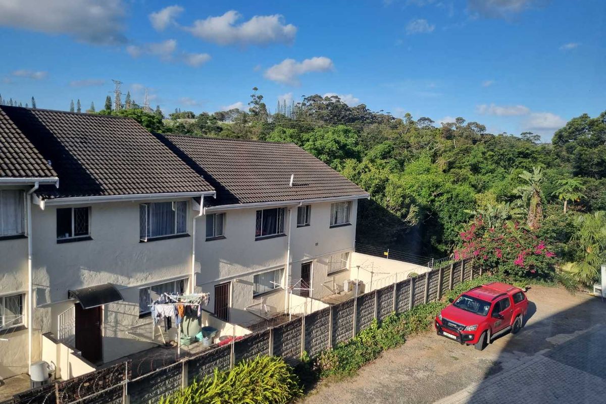 An elevated view of the rear exterior of a multi-story apartment complex, featuring tiled roofing, paved ground areas, and surrounding greenery.