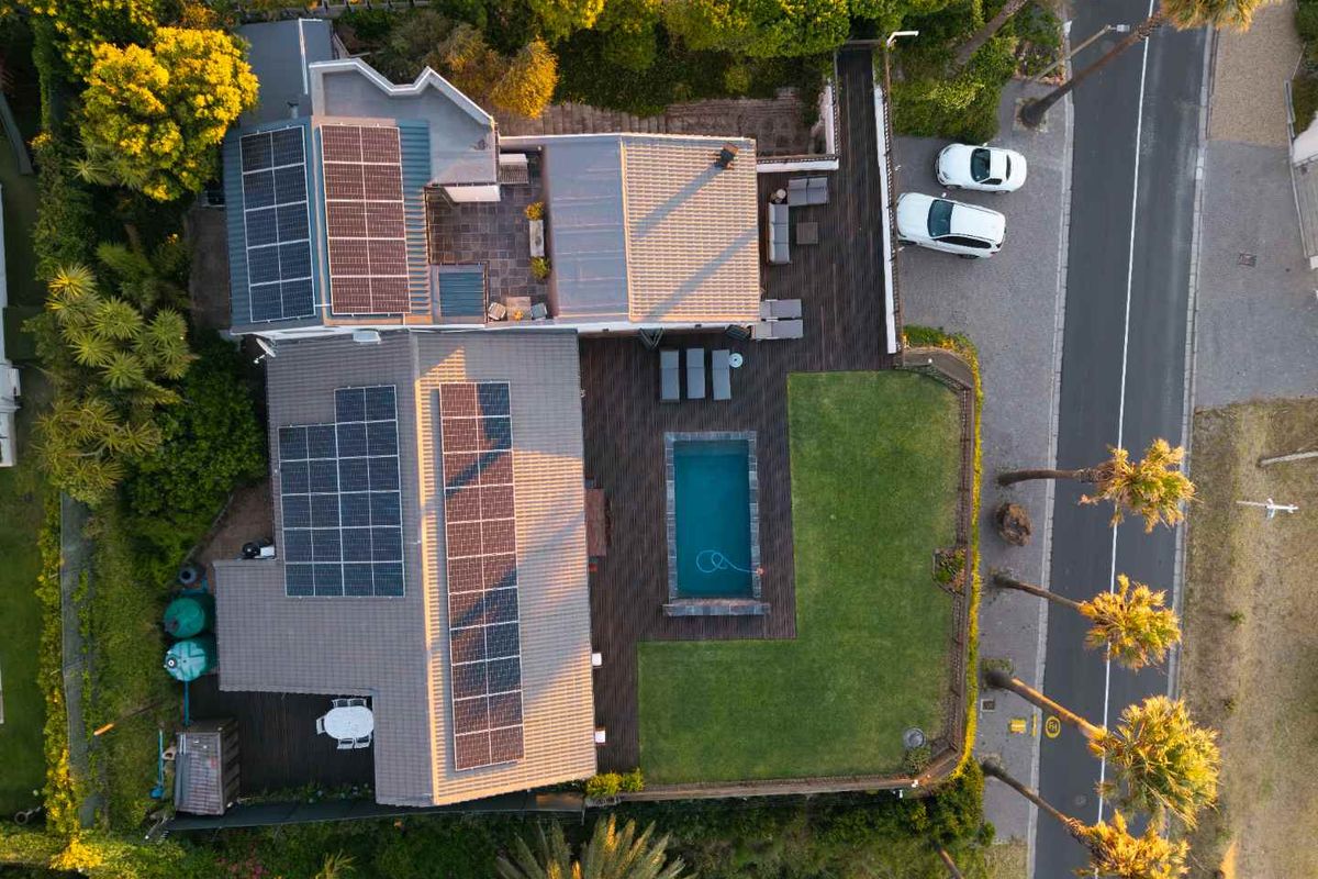 Aerial view of the property featuring a tiled roof with extensive solar panel installation, a swimming pool, timber decking, and a well-maintained garden.