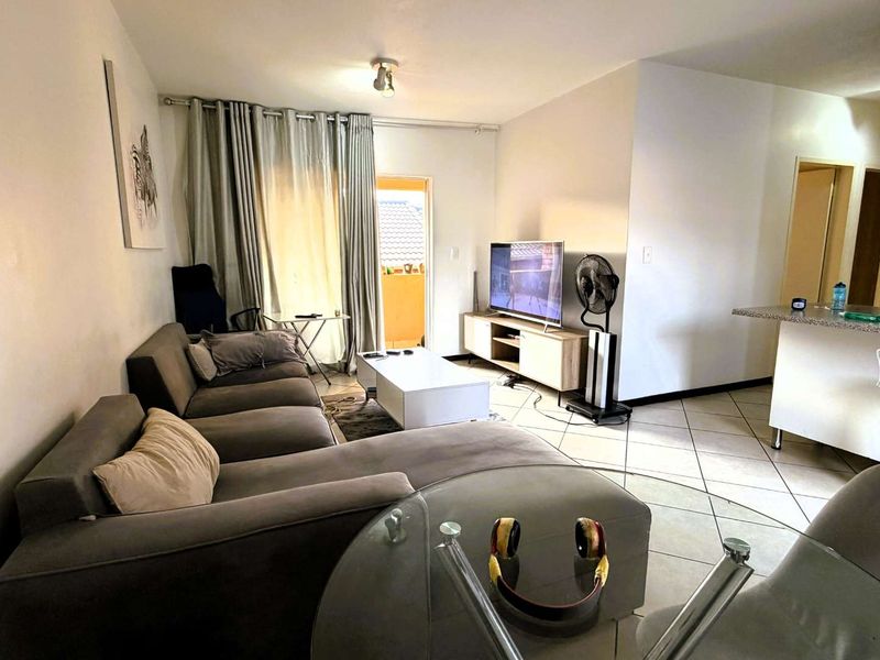 Open-plan living area featuring tiled flooring, a breakfast bar, and direct access to a balcony through a sliding door.