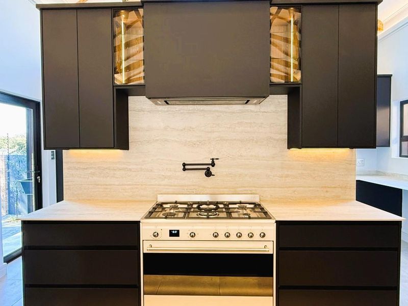Modern kitchen featuring dark cabinetry, a stone backsplash, a gas stove with oven, and a convenient wall-mounted pot filler tap.