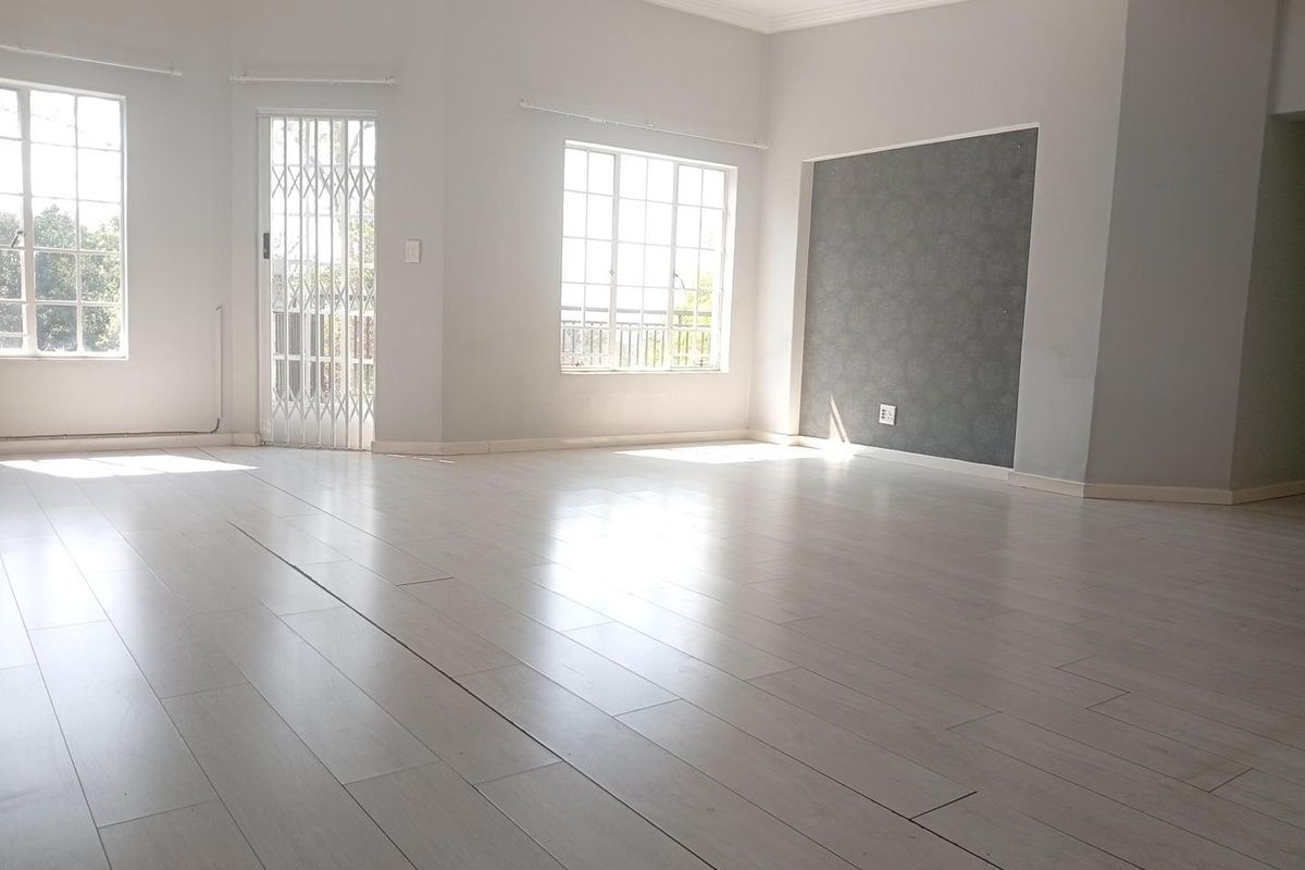 A bright, empty living area featuring light-toned laminate flooring, large windows, and a decorative accent wall, providing a clean canvas for interior design.