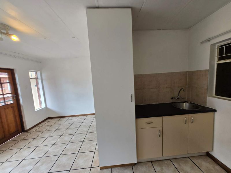 An open-plan living and kitchen area featuring tiled flooring, a compact kitchenette with built-in cabinetry, and direct access to an exterior door.