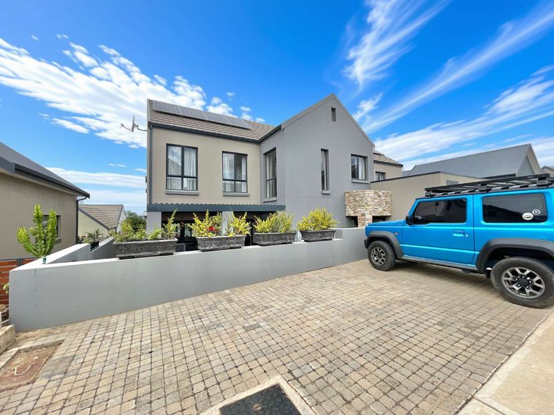 Modern double-storey residential property featuring a paved driveway, stone-clad accents, and solar panels on the roof.