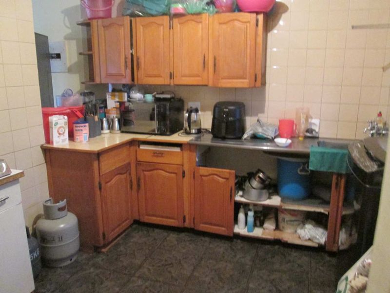 A dated kitchen featuring wooden cabinetry, tiled splashbacks, and a stainless steel sink, currently requiring cosmetic updates and repairs to the cabinetry.