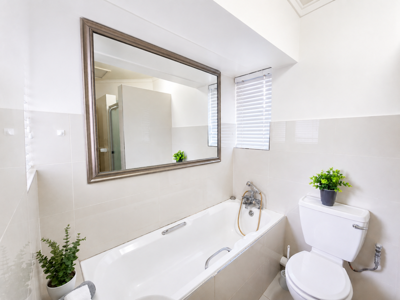 A clean, well-maintained bathroom featuring a built-in bathtub, wall-mounted mirror, and neutral wall tiling.