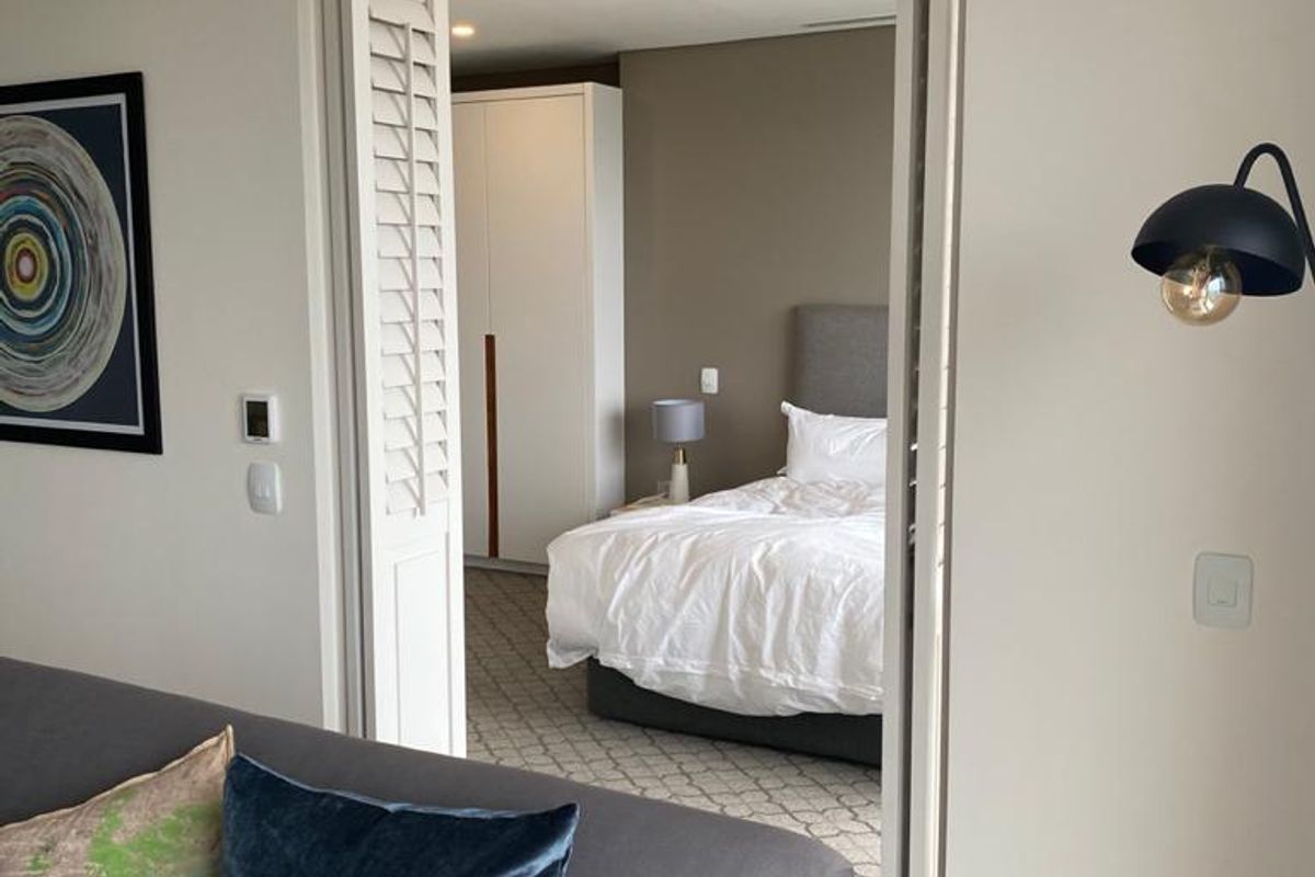 A view from the living area into a bedroom featuring built-in cabinetry and neutral carpeting, connected by folding shutter doors.