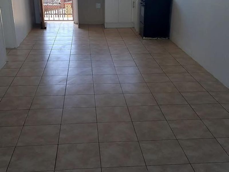 An open-plan living and kitchen area featuring tiled flooring, basic cabinetry, and a security gate leading to an outdoor space.