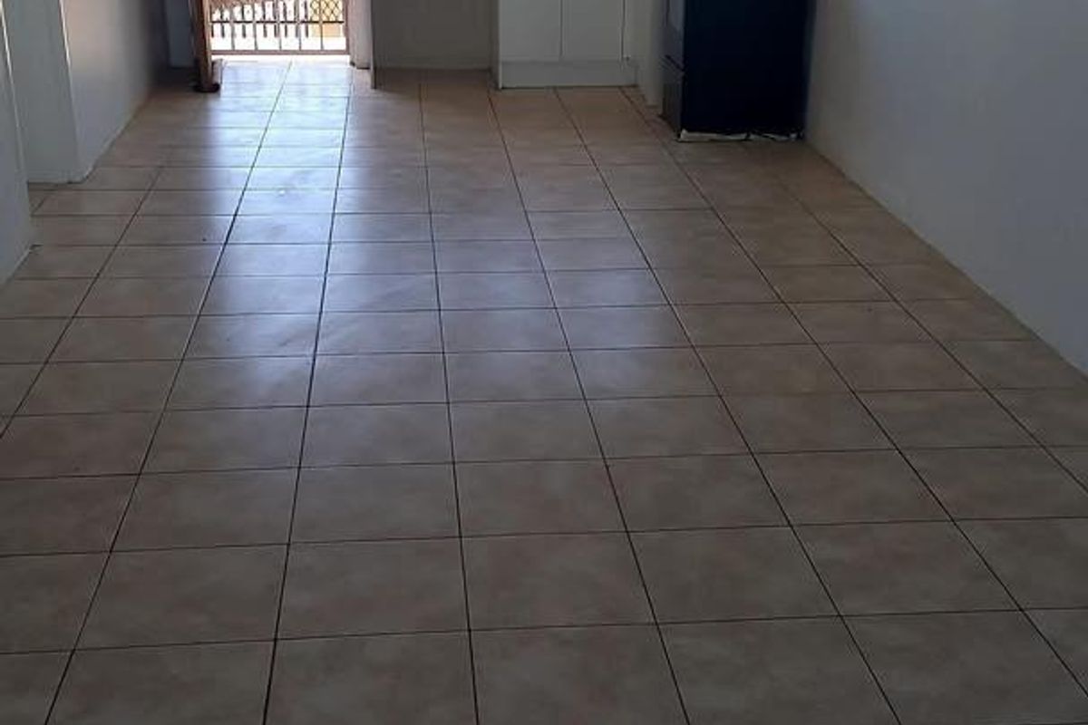 An open-plan living and kitchen area featuring tiled flooring, basic cabinetry, and a security gate leading to an outdoor space.